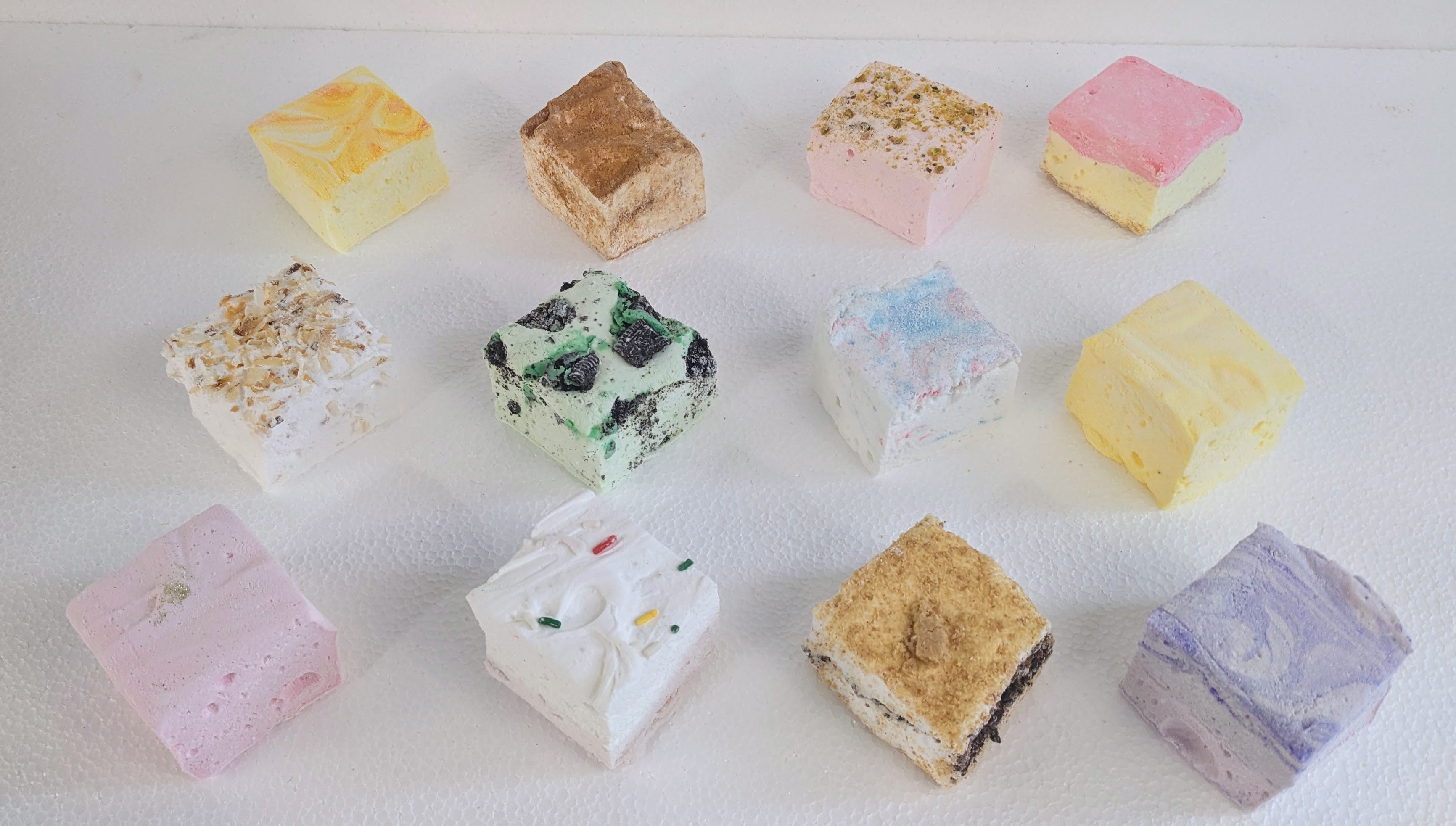 Assorted gourmet marshmallows in various colors and flavors spread out on a white background