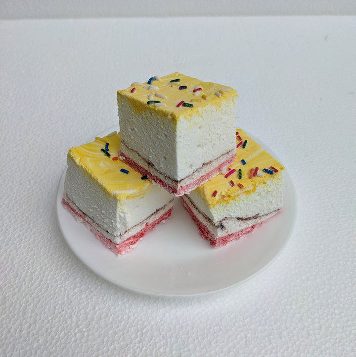 A close-up of three banana split gourmet marshmallows, displayed on a clean white background to emphasize their vibrant colors. Each marshmallow is handcrafted in the USA, featuring yellow, red, and brown swirls that highlight the classic banana, strawberry, and chocolate flavors. Topped with colorful sprinkles, these best-in-class artisanal marshmallows boast a soft, fluffy texture—perfect for desserts, s’mores, gifting, and luxury confections.