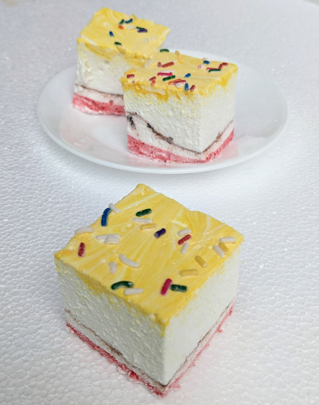 A close-up of three banana split gourmet marshmallows, arranged with one marshmallow in front and two slightly behind, creating depth and visual interest against a clean white background. Each marshmallow is handcrafted in the USA, featuring yellow, red, and brown swirls representing the iconic banana, strawberry, and chocolate flavors. Lightly dusted with colorful sprinkles, these best-in-class artisanal marshmallows showcase their soft, fluffy texture, making them perfect for desserts, s’mores, gifting, a