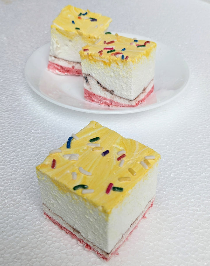 A close-up of three banana split gourmet marshmallows, arranged with one marshmallow in front and two slightly behind, creating depth and visual interest against a clean white background. Each marshmallow is handcrafted in the USA, featuring yellow, red, and brown swirls representing the iconic banana, strawberry, and chocolate flavors. Lightly dusted with colorful sprinkles, these best-in-class artisanal marshmallows showcase their soft, fluffy texture, making them perfect for desserts, s’mores, gifting, a