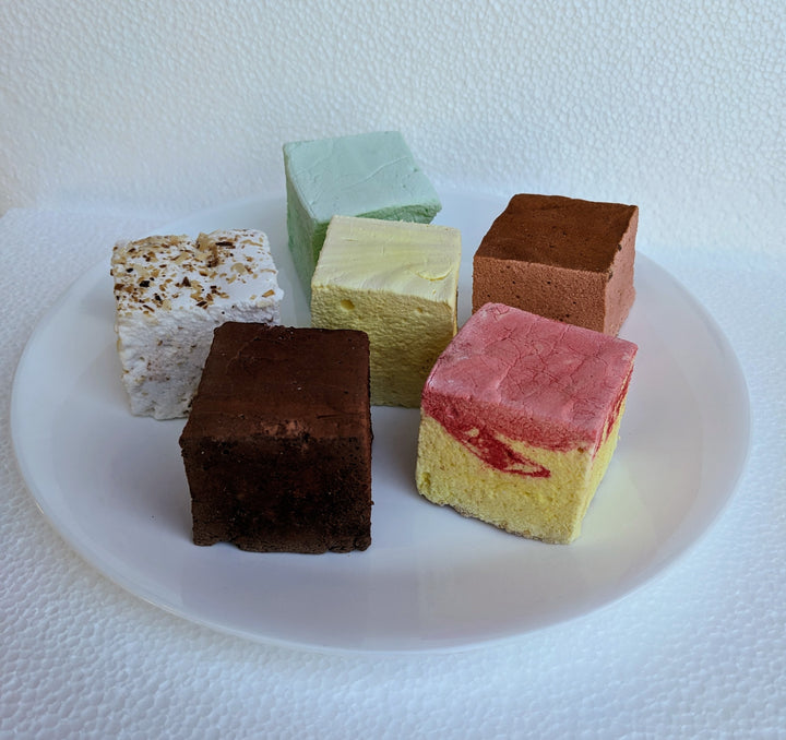 An inviting assortment of our best-selling gourmet marshmallows presented on a simple, clean white plate. The vibrant, fluffy marshmallows in various flavors and colors are beautifully arranged, highlighting their enticing textures and visual appeal