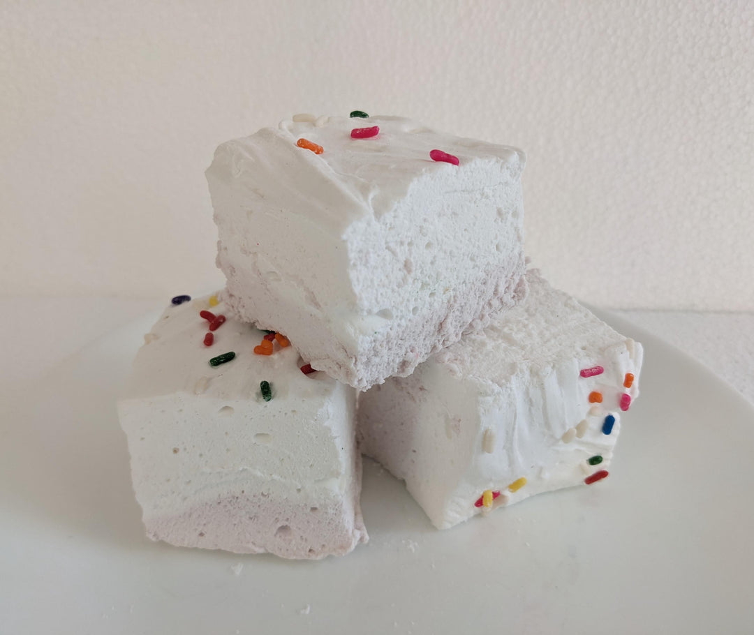 Birthday cake flavored marshmallows with a yellow bottom layer and white top layer, adorned with colorful sprinkles. The marshmallows are displayed on a clean, white background, featuring The Toasty Smore logo and a "Made in USA" flag.