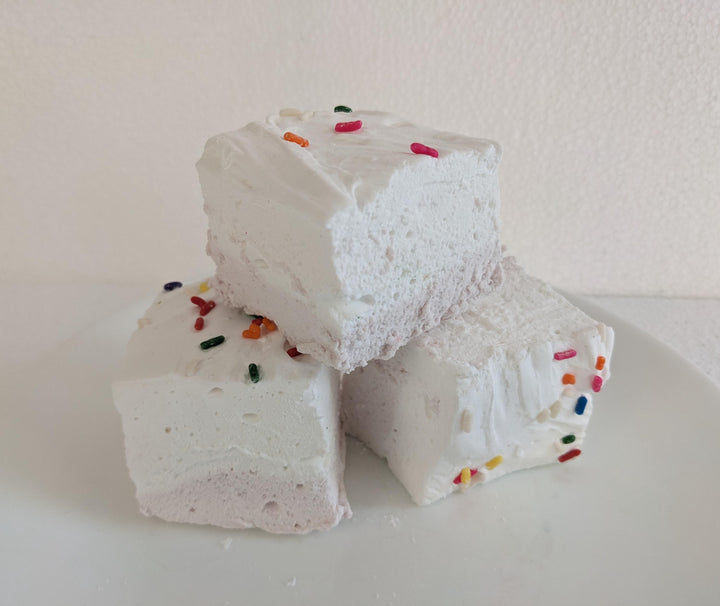 Birthday cake flavored marshmallows with a yellow bottom layer and white top layer, adorned with colorful sprinkles. The marshmallows are displayed on a clean, white background, featuring The Toasty Smore logo and a "Made in USA" flag.