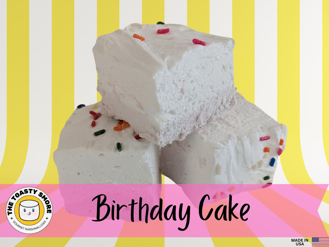 Birthday cake flavored marshmallows with a yellow bottom layer and white top layer, adorned with just a few colorful sprinkles. The marshmallows are displayed on a yellow and white striped background, featuring The Toasty Smore logo and a "Made in USA" flag.