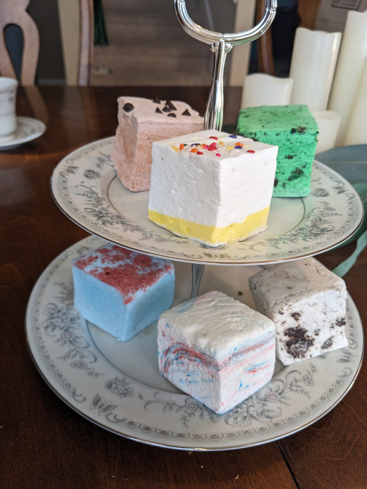 A two-tiered plate featuring a vibrant assortment of birthday-themed marshmallows in flavors: birthday cake, cotton candy, blue raspberry, cookie dough, cookies & cream, and mint oreo.