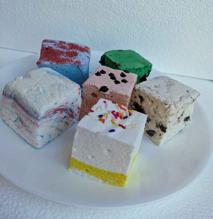 A white plate featuring a vibrant assortment of birthday-themed marshmallows in flavors: birthday cake, cotton candy, blue raspberry, cookie dough, cookies & cream, and mint oreo.