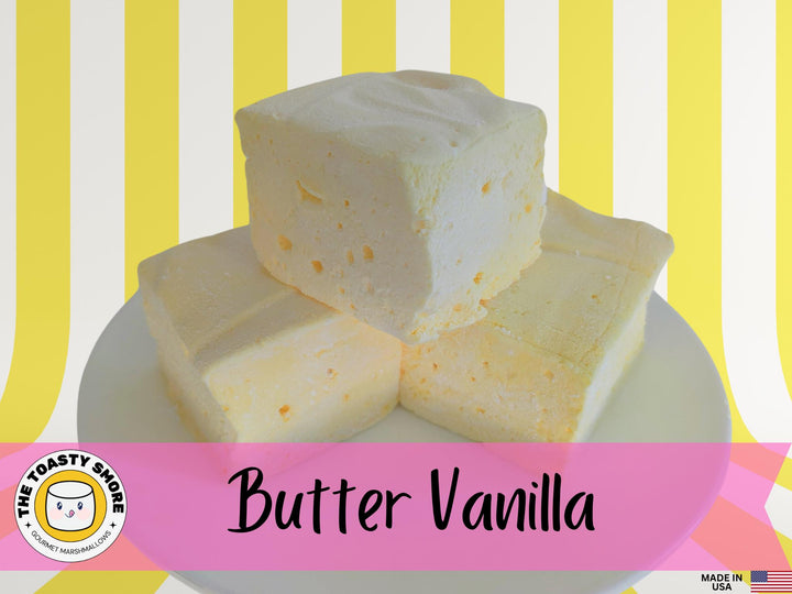 Three extra-large Butter Vanilla gourmet marshmallows made with organic marshmallow root and premium beef gelatin, displayed on a white plate against a yellow and white striped background. The image includes The Toasty S’more logo and a “Made in USA” flag