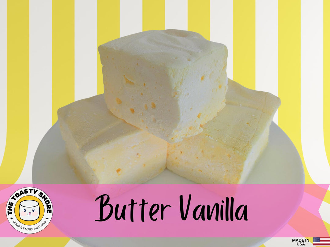 Three butter vanilla marshmallows on a white plate, displayed against a yellow and white striped background. The image features The Toasty Smore logo and a "Made in USA" flag.