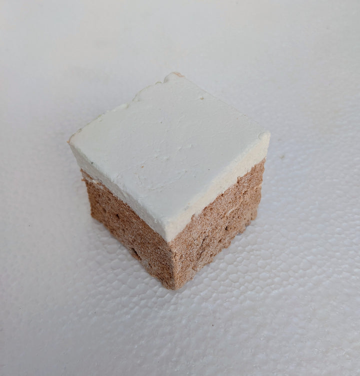 A single, golden Butterbeer marshmallow sits at the front of a clean, white plate, with two more fluffy cubes behind it. Its butterscotch shimmer catches the light, highlighting its pillowy texture. Handmade in the USA with premium gelatin and no corn syrup, this gourmet marshmallow is perfect for s’mores, snacking, or gifting. 
