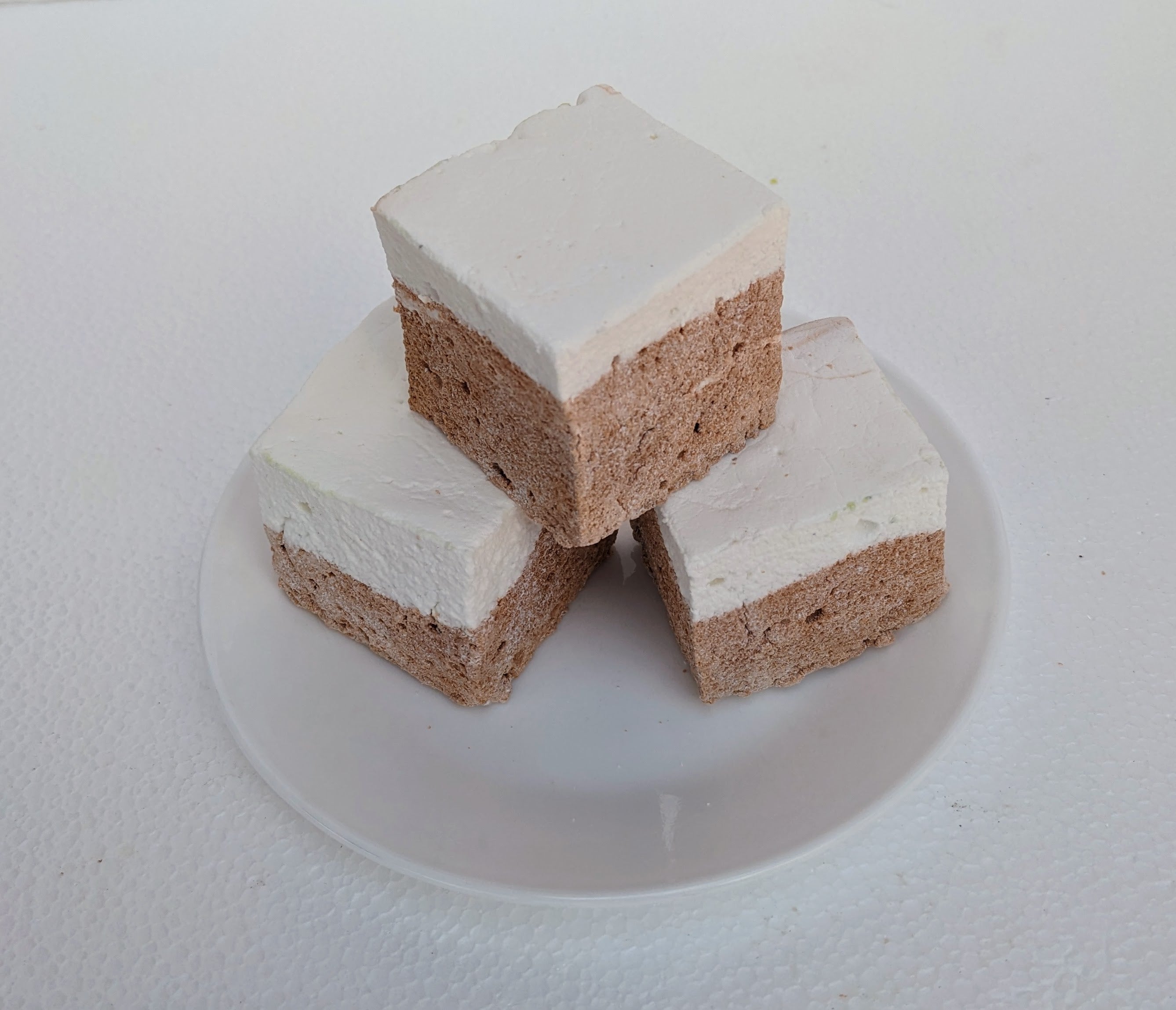 Three large, fluffy Butterbeer marshmallows sit on a clean, white plate, their golden butterscotch cubes gleaming with a light shimmer. Handmade with premium gelatin and no corn syrup, these gourmet marshmallows are perfect for s’mores, desserts, or gifting.
