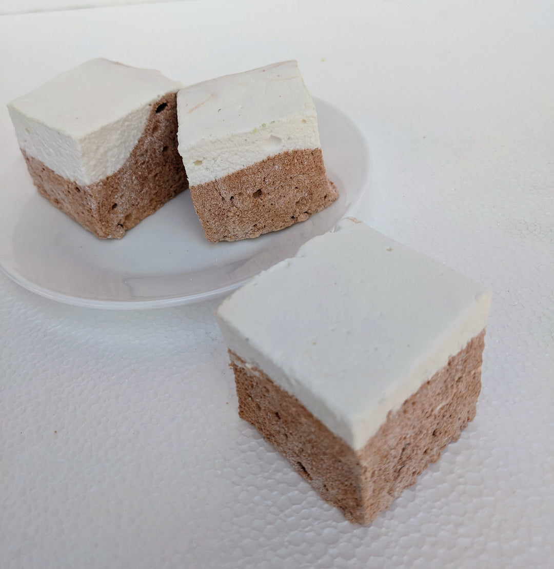 Three golden Butterbeer marshmallows sit on a clean, white plate, with one slightly in front, showcasing its pillowy texture. Each extra-large 2-inch cube is handcrafted in the USA, made with premium gelatin and no corn syrup for the perfect melt-in-your-mouth experience. Their butterscotch-vanilla essence shines, making them ideal for s’mores, desserts, or gourmet gifting.
