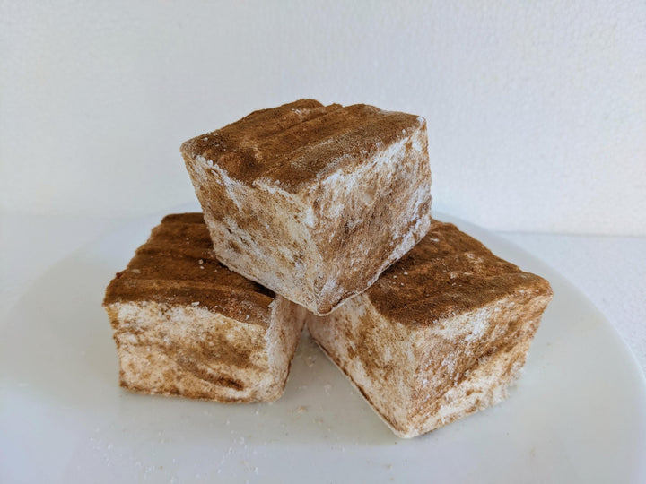 Three caramel churro marshmallows on a white plate, displayed on a plain white background.