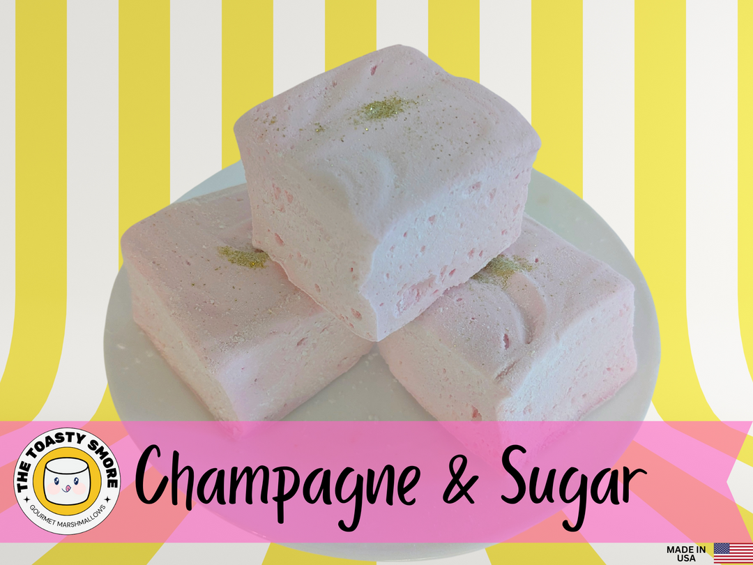 Plate of Champagne and Sugar Flavored Gourmet Marshmallows that are a light pink color with a dab of edible gold glitter in the center of each marshmallow – Delicious Handcrafted Treats with yellow and white striped background with The Toasty Smore Logo,  and Made in USA Flag at the Bottom