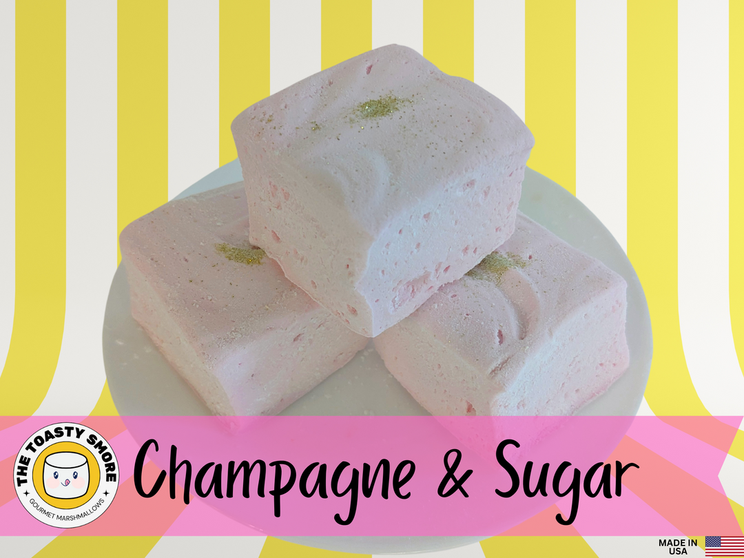 Light pink Champagne and Sugar marshmallows made with beef gelatin, organic marshmallow root, and no corn syrup, each topped with edible gold glitter and arranged on a plate against a yellow and white striped background. The Toasty S’more logo and a “Made in USA” flag are featured at the bottom, highlighting handcrafted quality and clean-label ingredients.
