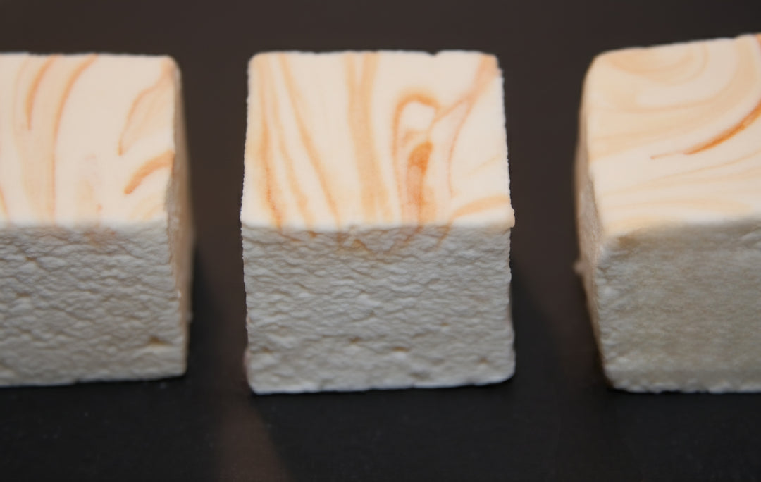 Close-up of three Lemon Pound Cake marshmallows by The Toasty S’more topped with lemon zest, styled on a dark surface with fresh lemons and a sliced pound cake in the background. Handcrafted, corn-syrup free, and made with beef gelatin and organic marshmallow root for a clean-label indulgence.