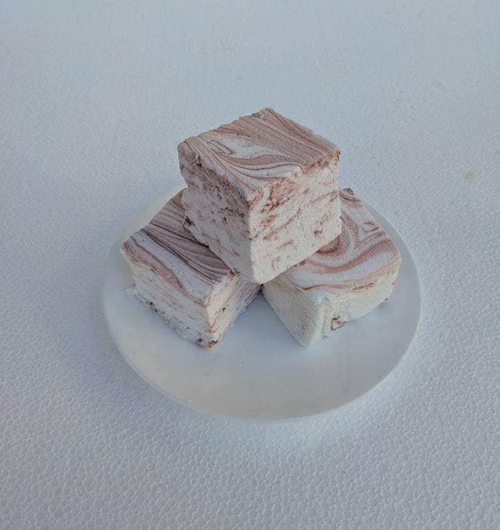 A close-up view of coffee-flavored gourmet marshmallows, handcrafted and made in the USA by The Toasty Smore, arranged on a white plate. Each marshmallow is white with rich brown swirls, creating a marbled effect that showcases the bold coffee infusion. Their soft, fluffy texture contrasts beautifully with the smooth, swirled design, emphasizing their artisanal quality. Perfect for coffee lovers, these best gourmet marshmallows offer a delicious balance of sweetness and deep coffee flavor, ideal for pairing