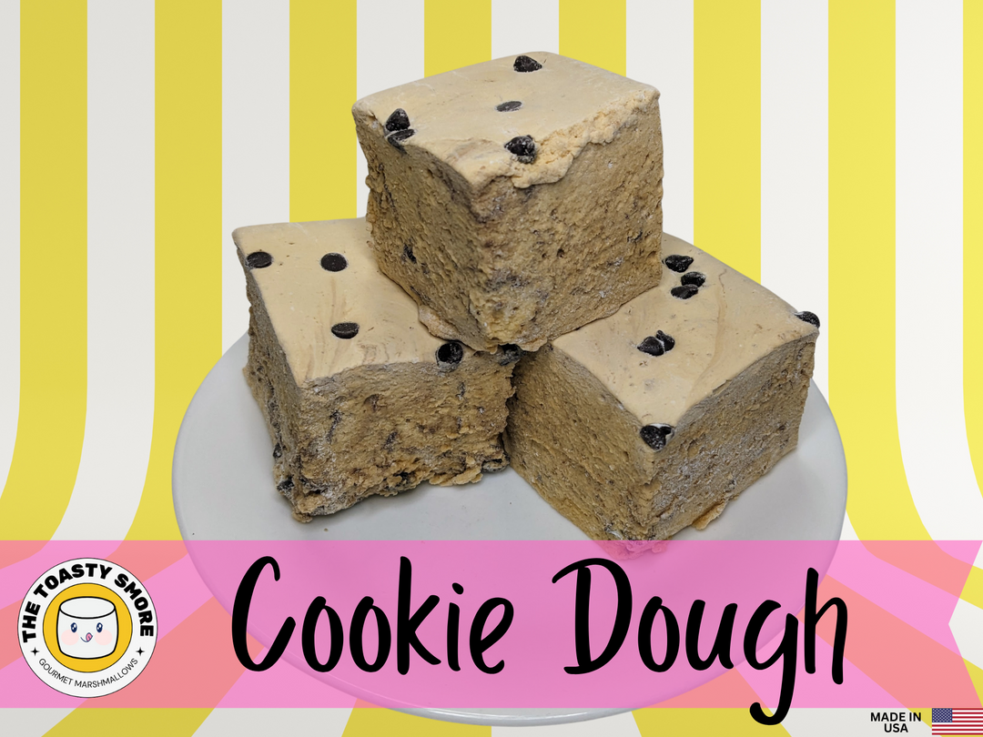 Three cookie dough marshmallows on a white plate, displayed on a yellow and white striped background. The image features The Toasty Smore logo and a "Made in USA" flag.