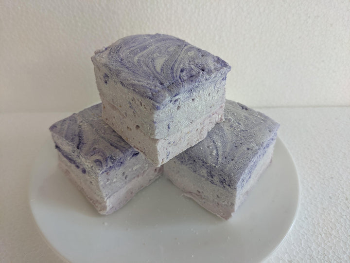 Three creamy purple taro marshmallows on a white plate, displayed on a plain white background.