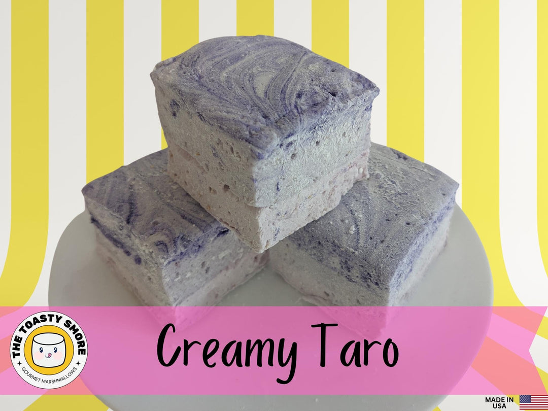 Three creamy purple taro marshmallows on a white plate, set against a yellow and white striped background. The marshmallows are displayed with The Toasty Smore logo and a "Made in USA" flag.