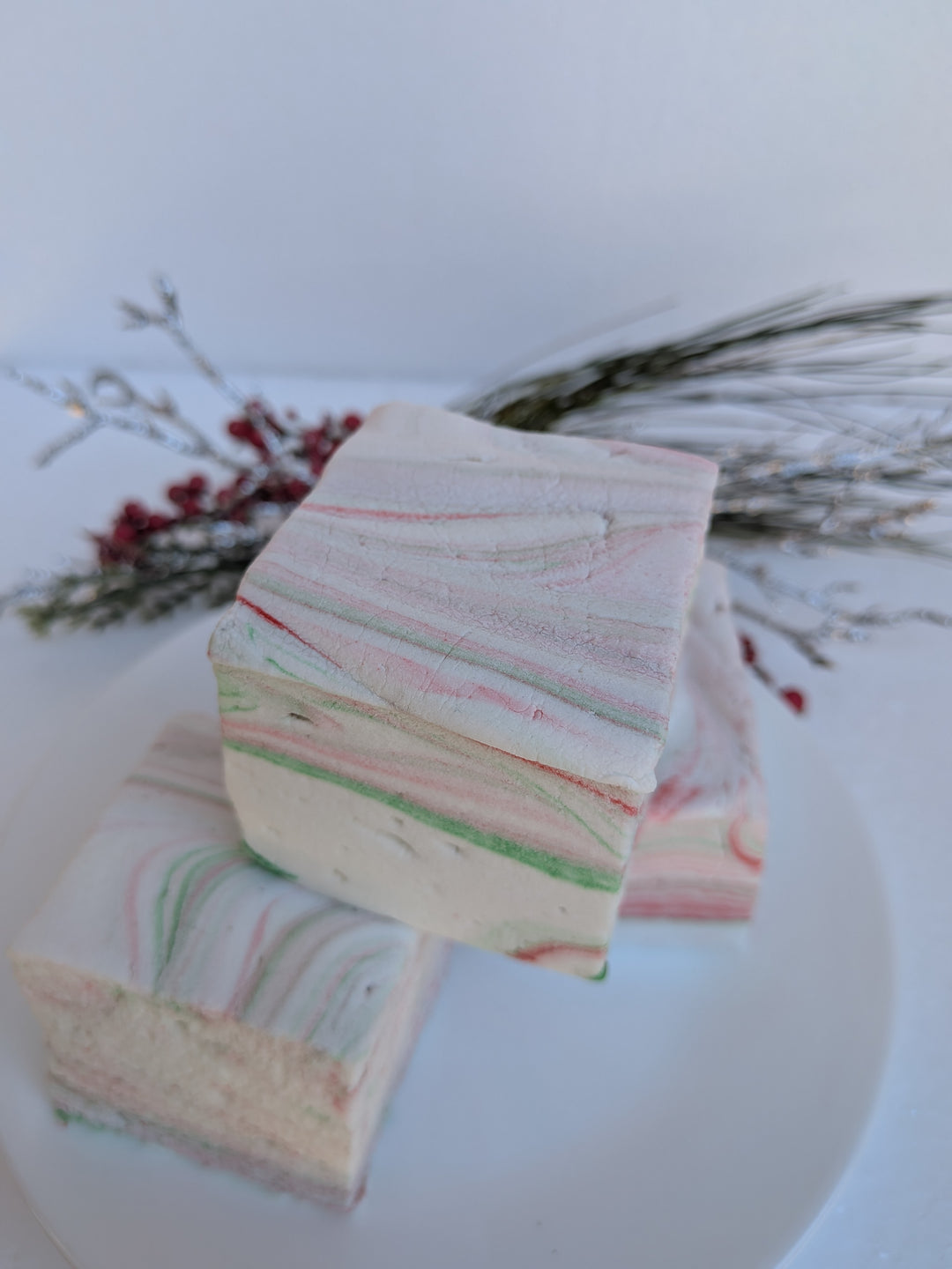 Stack of three White Chocolate Peppermint Bark marshmallows by The Toasty S’more, styled with festive Christmas greenery on a white background. Handcrafted with beef gelatin and organic marshmallow root for a corn-syrup free, clean-label holiday treat.