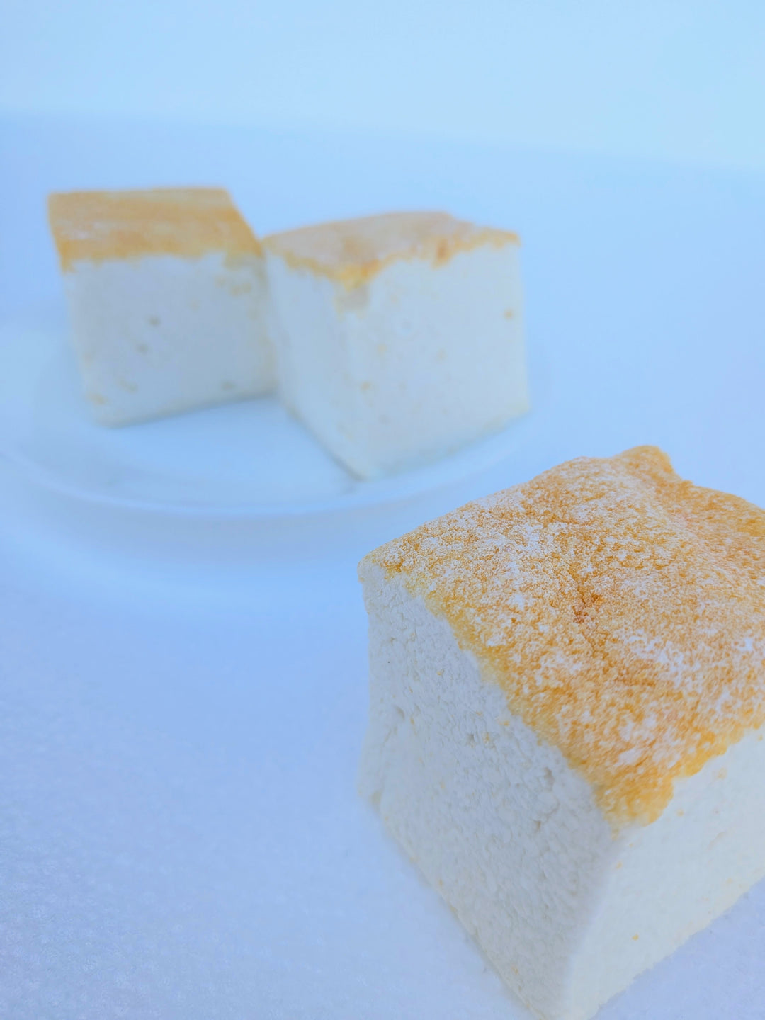 Three fluffy Piña Colada marshmallows with toasted tops, one in the foreground and two on a clear plate, made with beef gelatin and organic marshmallow root; clean‑label, corn‑syrup free real marshmallows.