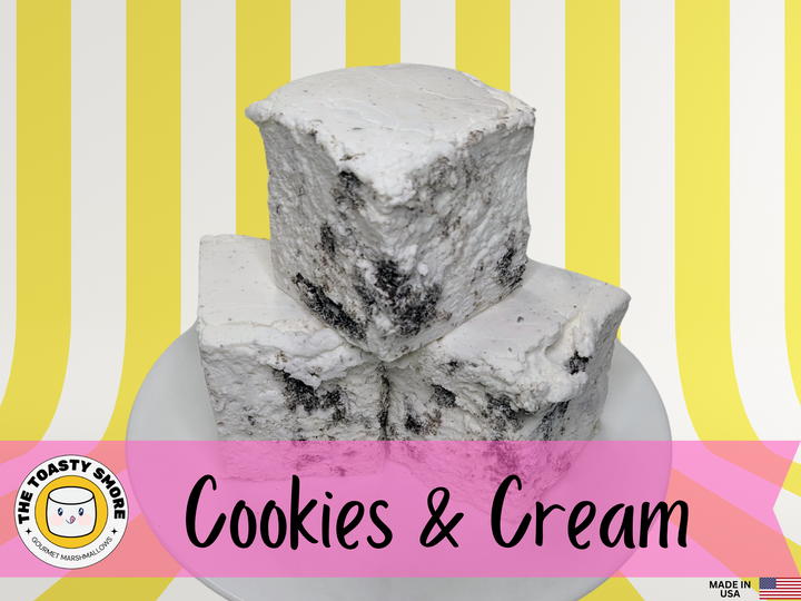 Three handcrafted gourmet cookies & cream marshmallows on a white plate, displayed against a yellow and white striped background. The marshmallows are approximately 2" x 2" x 1.5" each and made from premium gelatin. The image features The Toasty Smore logo and a "Made in USA" flag.