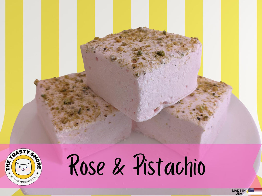 Three handcrafted gourmet rose and pistachio marshmallows, neatly placed on a white plate and displayed against a yellow and white background. Each marshmallow is approximately 2" x 2" x 1.5", crafted with high-quality beef gelatin. The image prominently features The Toasty Smore logo and a "Made in USA" flag.