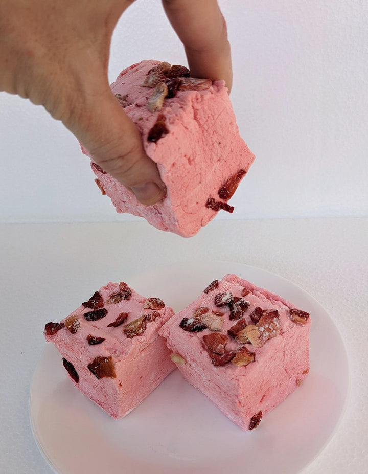Stack of Three Handcrafted Gourmet Strawberries in White Custard Sauce Marshmallows on a White Background. A hand is gently squeezing one of the marshmallows to show its softness and texture.