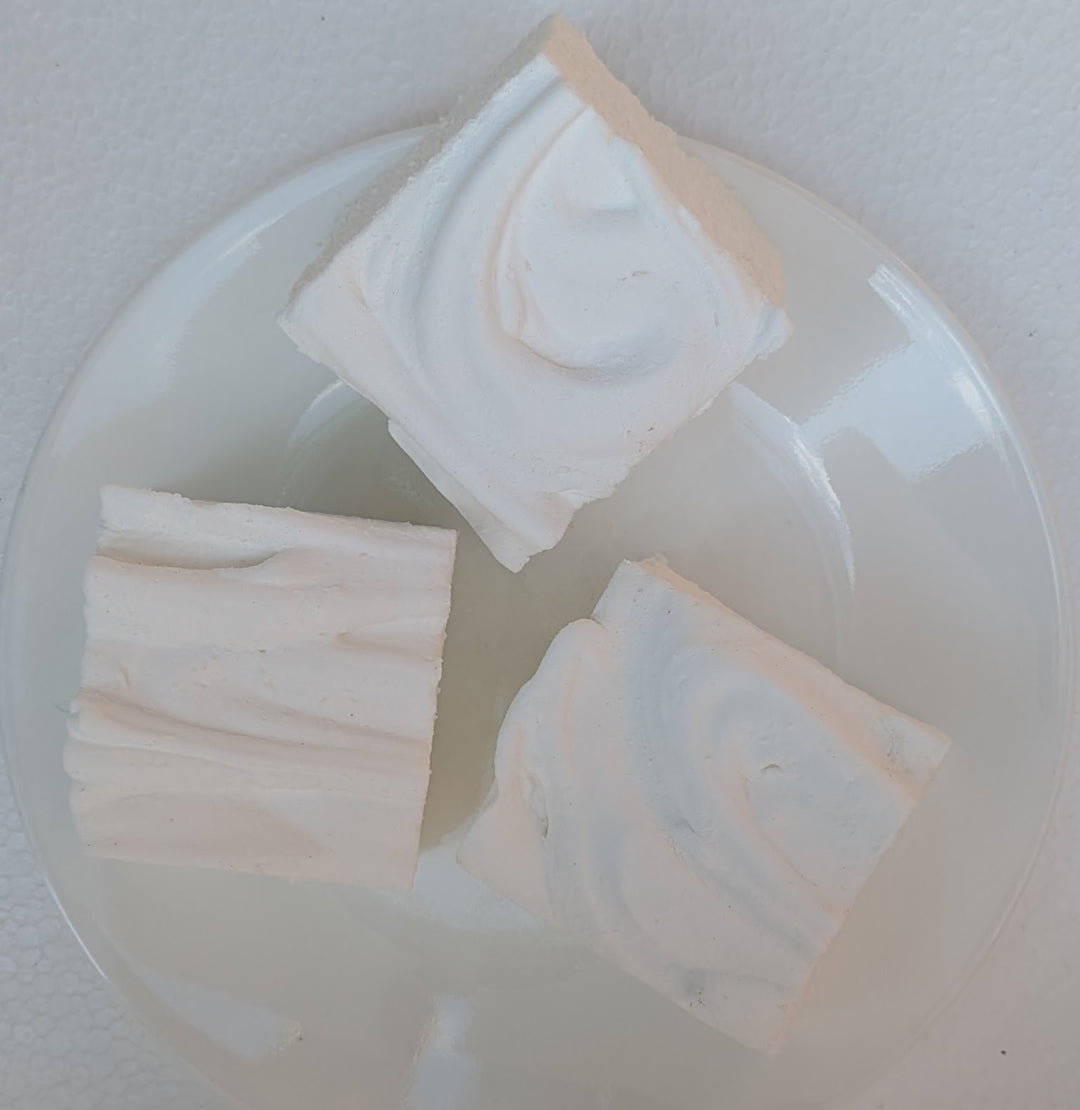 Three square pieces of Irish cream gourmet marshmallows on a clear plastic tray with a white background