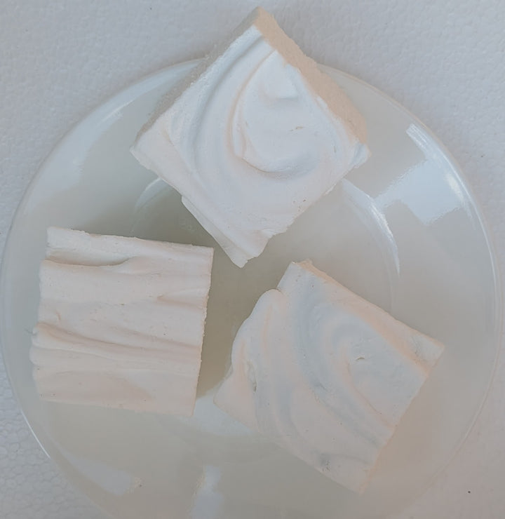 Three square pieces of Irish cream gourmet marshmallows on a clear plastic tray with a white background