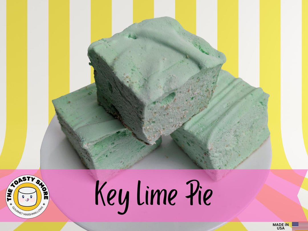 A plate of Key Lime Pie marshmallows is displayed on a yellow and white striped background. The marshmallows are light green squares dusted with golden graham cracker crumbs. The image features The Toasty Smore logo and a "Made in USA" flag.