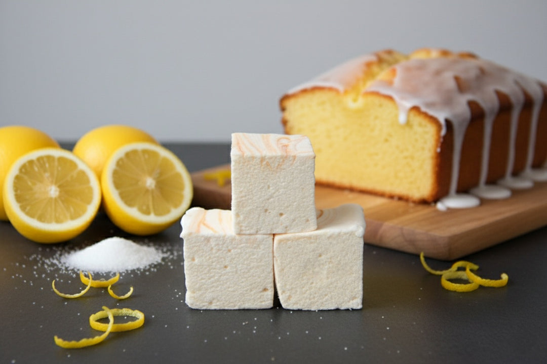 Three handcrafted Lemon Pound Cake marshmallows by The Toasty S’more styled with fresh lemon zest, set on a dark surface with whole lemons and a sliced pound cake in the background. Made with beef gelatin and organic marshmallow root for a corn-syrup free, clean-label treat.