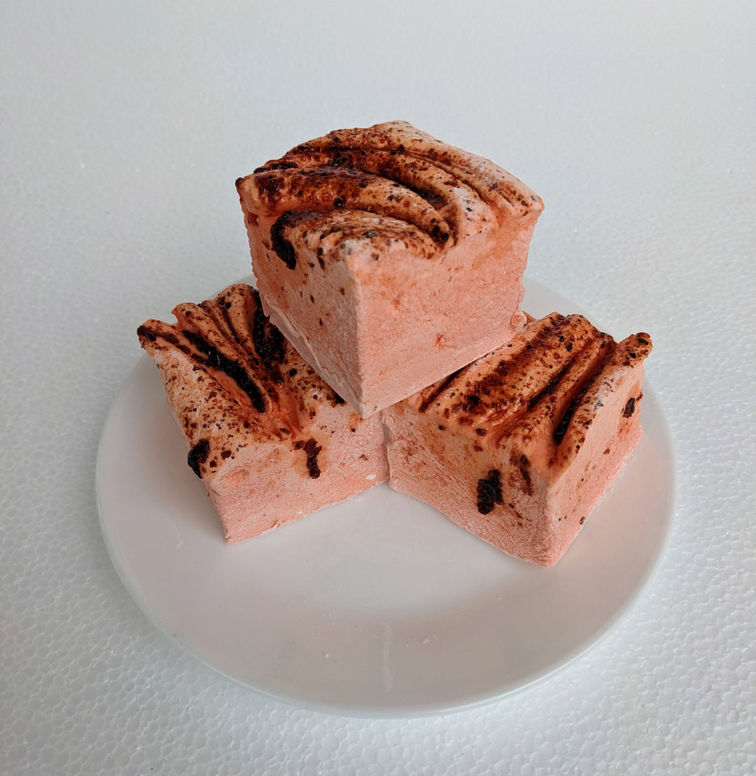 Three vibrant orange mango chamoy marshmallows on a white plate, displayed on a plain white background.