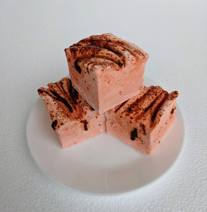 Three vibrant orange mango chamoy marshmallows on a white plate, displayed on a plain white background.