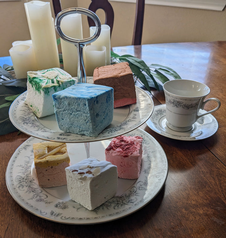 "A delectable selection of our Medieval Delight Bundle marshmallows elegantly displayed on a two-tiered fancy plate. Featuring flavors such as Red Rose Pudding, Gingerbread, Almond Cake, Junket with Blueberries, Pears in Wine Syrup, and Strawberries in White Custard Sauce