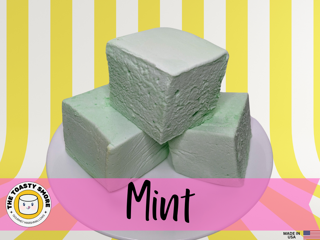 Three mint green marshmallows on a white plate, set against a yellow and white striped background. The marshmallows, made with premium gelatin, are displayed with The Toasty Smore logo and a "Made in USA" flag