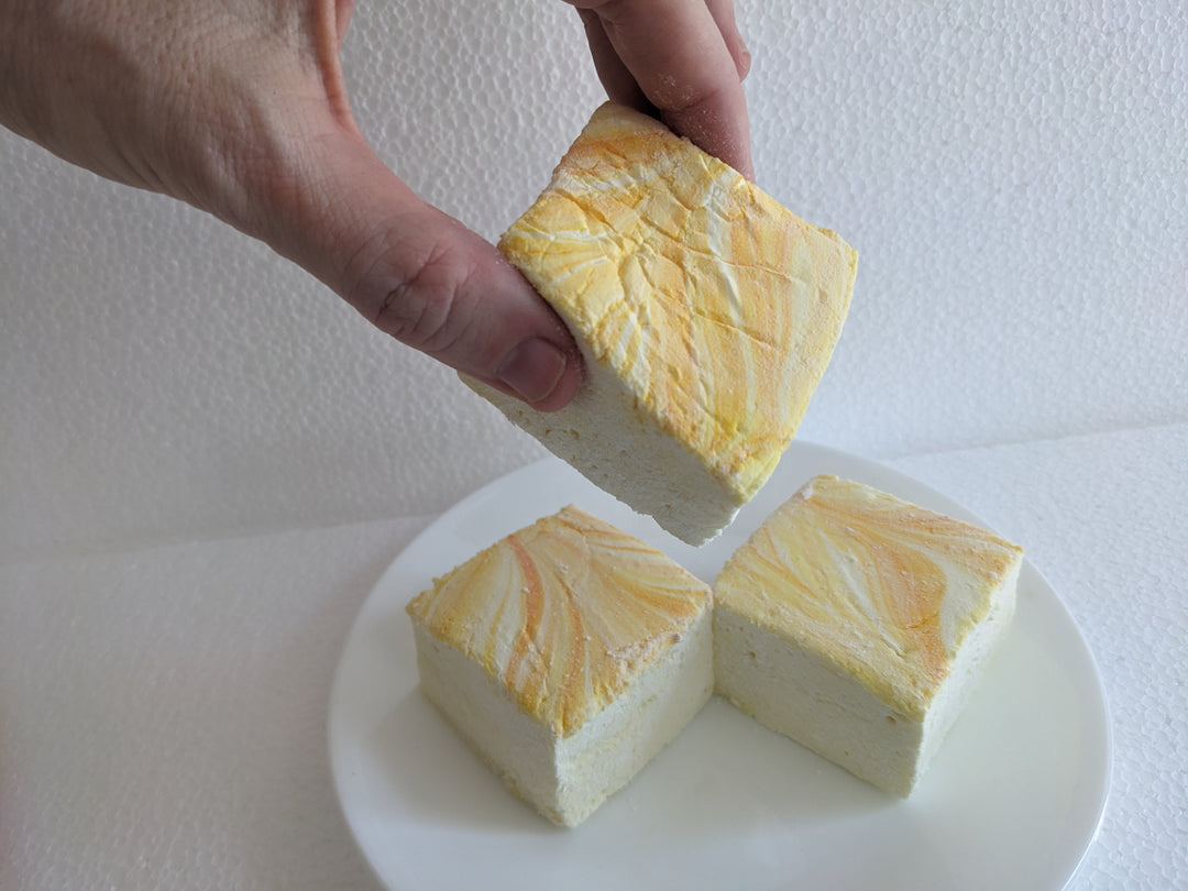 A hand picking up a Gourmet Handcrafted Lemon Pound Cake Marshmallow with white background