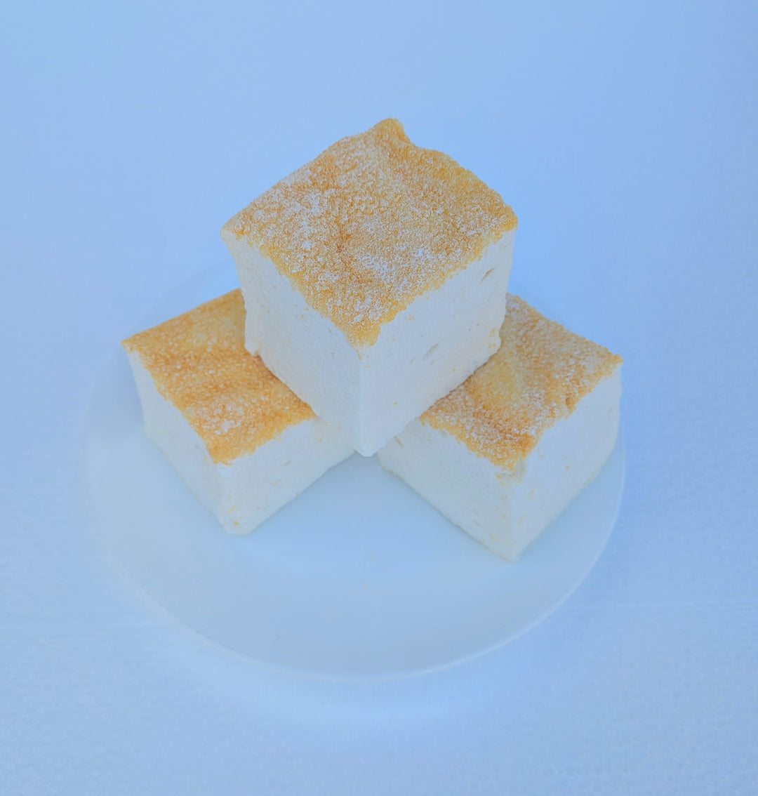 Three fluffy Piña Colada marshmallows on a white plate with toasted tops, made with beef gelatin and organic marshmallow root; clean‑label, corn‑syrup free real marshmallows.