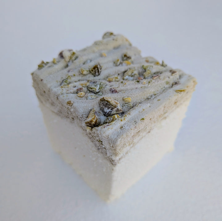 Close‑up of a pistachio marshmallow made with beef gelatin and organic marshmallow root, showing a pistachio‑studded top with a white base against a plain background. Clean‑label, gluten‑free, corn syrup‑free real marshmallows photographed in a detailed food shot.