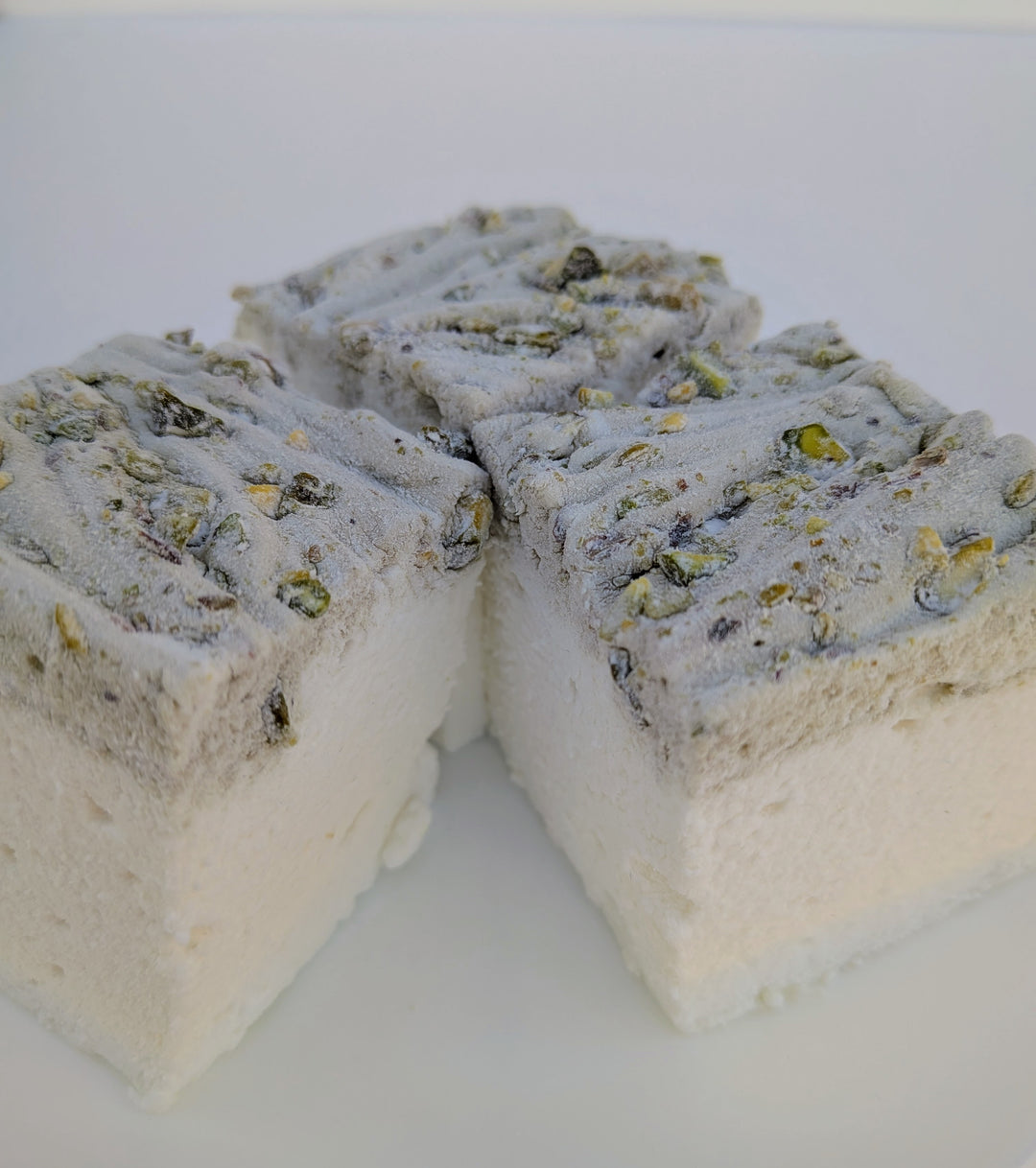 Three pistachio marshmallows made with beef gelatin and organic marshmallow root, arranged in a triangular stack with a textured pistachio‑studded top. Clean‑label, gluten‑free, corn syrup‑free real marshmallows photographed in a close‑up food shot.