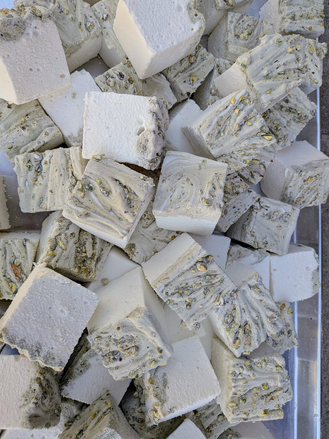 Pile of pistachio marshmallows made with beef gelatin and organic marshmallow root, showing a white base with a swirled pistachio‑studded top. Clean‑label, corn syrup‑free, gluten‑free real marshmallows photographed in a close‑up food shot.