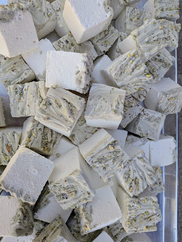 Pile of pistachio marshmallows made with beef gelatin and organic marshmallow root, showing a white base with a swirled pistachio‑studded top. Clean‑label, corn syrup‑free, gluten‑free real marshmallows photographed in a close‑up food shot.