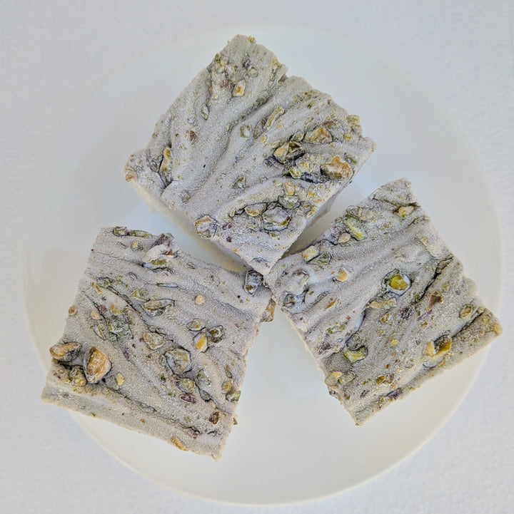 Three pistachio marshmallows made with beef gelatin and organic marshmallow root, arranged on a white plate with a textured pistachio‑studded top. Clean‑label, gluten‑free, corn syrup‑free real marshmallows photographed in a close‑up food shot.