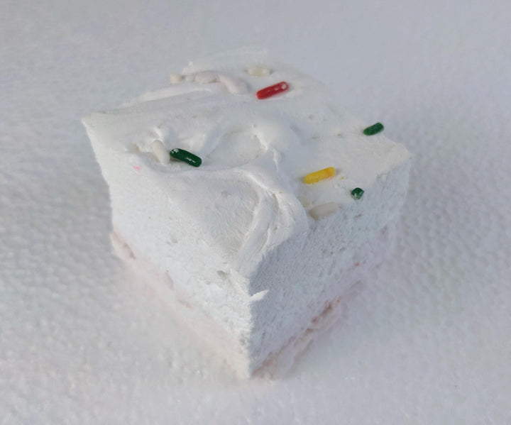 A single birthday cake flavored marshmallow with a yellow bottom layer and white top layer, adorned with sparse colorful sprinkles. The marshmallow is displayed on a clean, white background