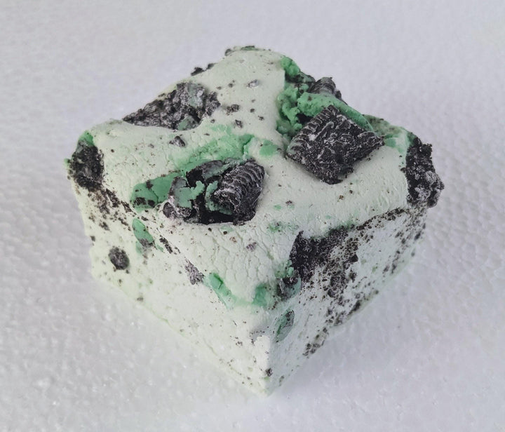 A single mint green marshmallow with Oreo crumbs on a white plate, displayed on a plain white background.