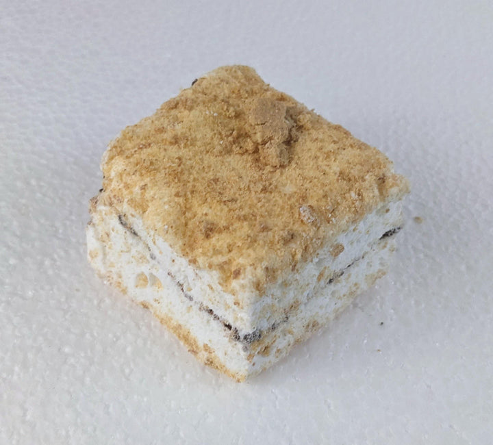A single s'mores marshmallow showcased on a clean, white background. The marshmallow is perfectly toasted to a golden brown, with a slightly melted, rich semi-sweet chocolate layer beneath it, and a crisp graham cracker on the bottom. The details highlight the fluffy, airy texture of the marshmallow, and the contrast with the gooey chocolate and crunchy graham cracker. The simplicity of the white background emphasizes the mouthwatering appeal of this classic treat.