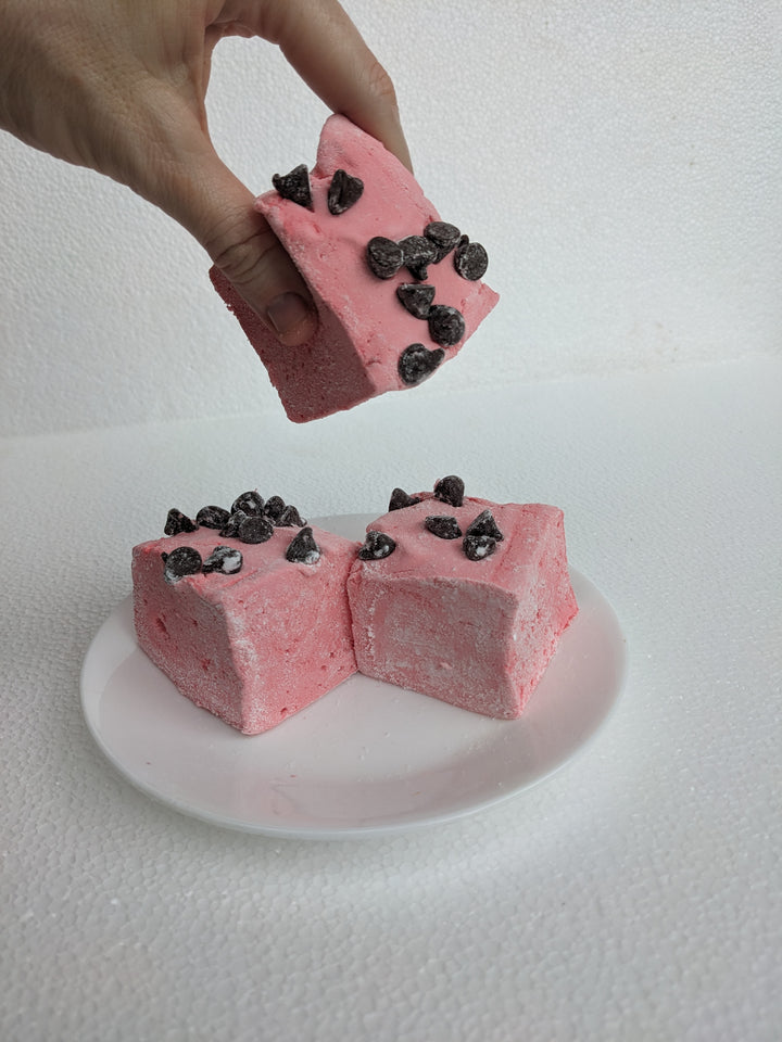 A hand picks up a single Gourmet Handcrafted Wild Cherry Chip Marshmallow and squeezes it for squish test