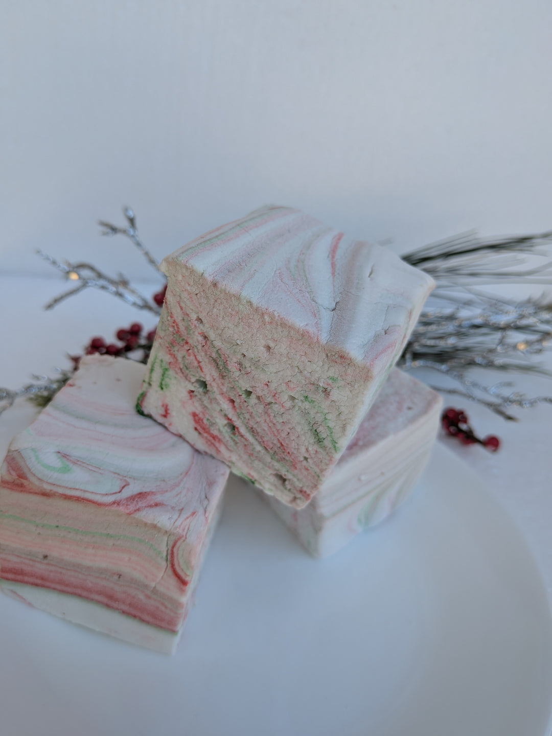 Three stacked White Chocolate Peppermint Bark marshmallows by The Toasty S’more, set against a white background with festive Christmas greenery. Handcrafted with beef gelatin and organic marshmallow root for a corn-syrup free, clean-label seasonal treat.
