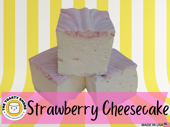 Three handcrafted strawberry cheesecake marshmallows made with natural colors, Halal‑certified beef gelatin, organic marshmallow root, and clean‑label ingredients, shown on a vibrant yellow and white striped background. These corn‑syrup‑free,  real marshmallows display a soft, fluffy texture with rich cheesecake flavor and strawberry accents, alongside The Toasty S’more logo and a Made in USA flag to emphasize artisanal quality and ingredient integrity.
