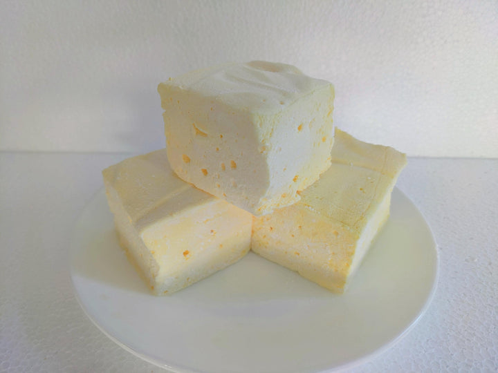 Three butter vanilla flavored marshmallows, displayed on a clean, white background. Each marshmallow has a light yellow hue, embodying the classic colors associated with butter vanilla. The soft, fluffy texture and uniform shape of the marshmallows emphasize the artisanal quality and delightful appearance of these gourmet treats.